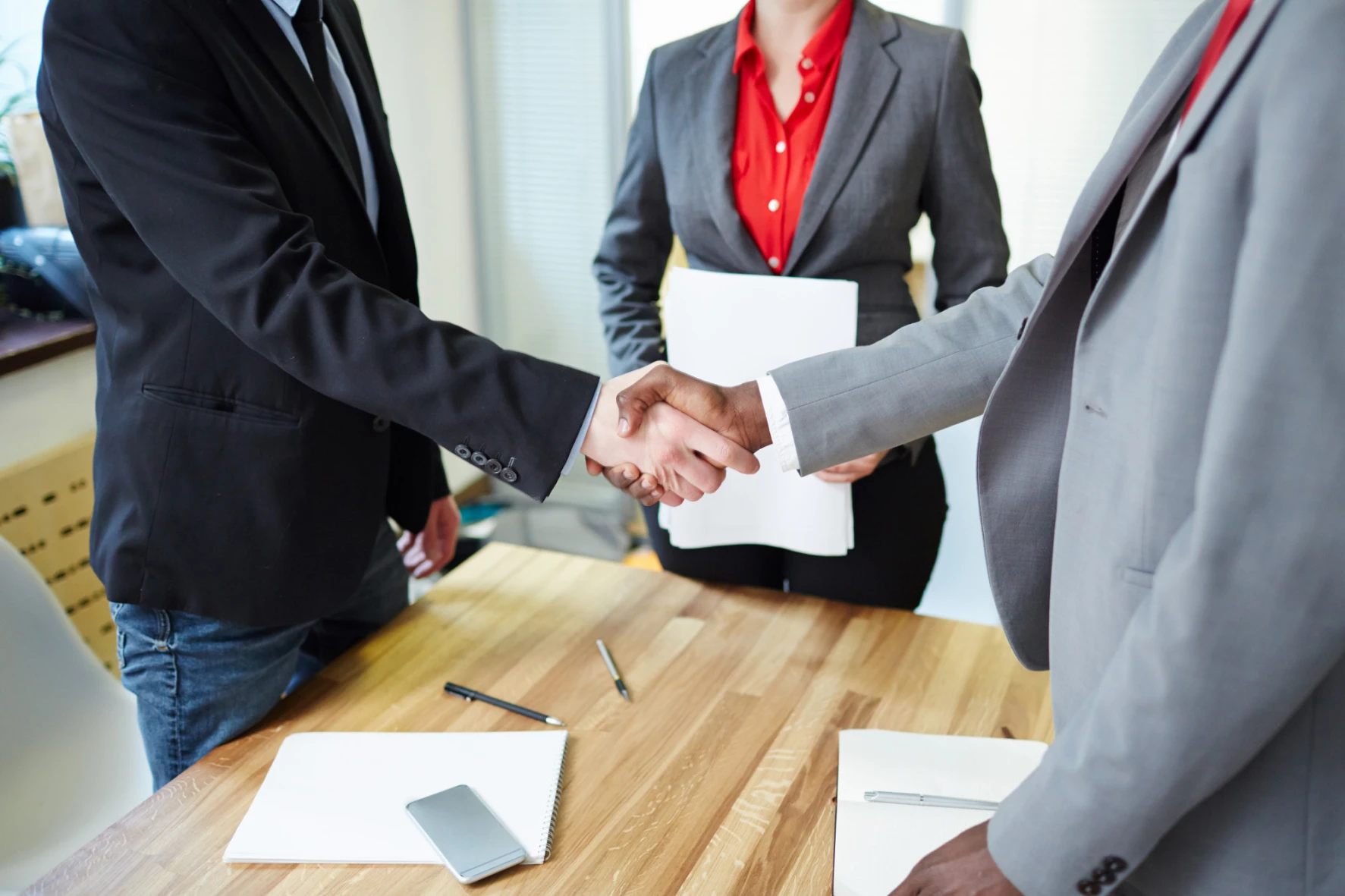 3 business people, with 2 shaking hands